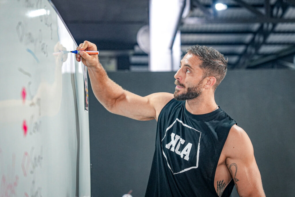 Peter Forneck teaching in front of a whiteboard during the KCA Level 3 “Teach the Kettlebell” instructor certification.